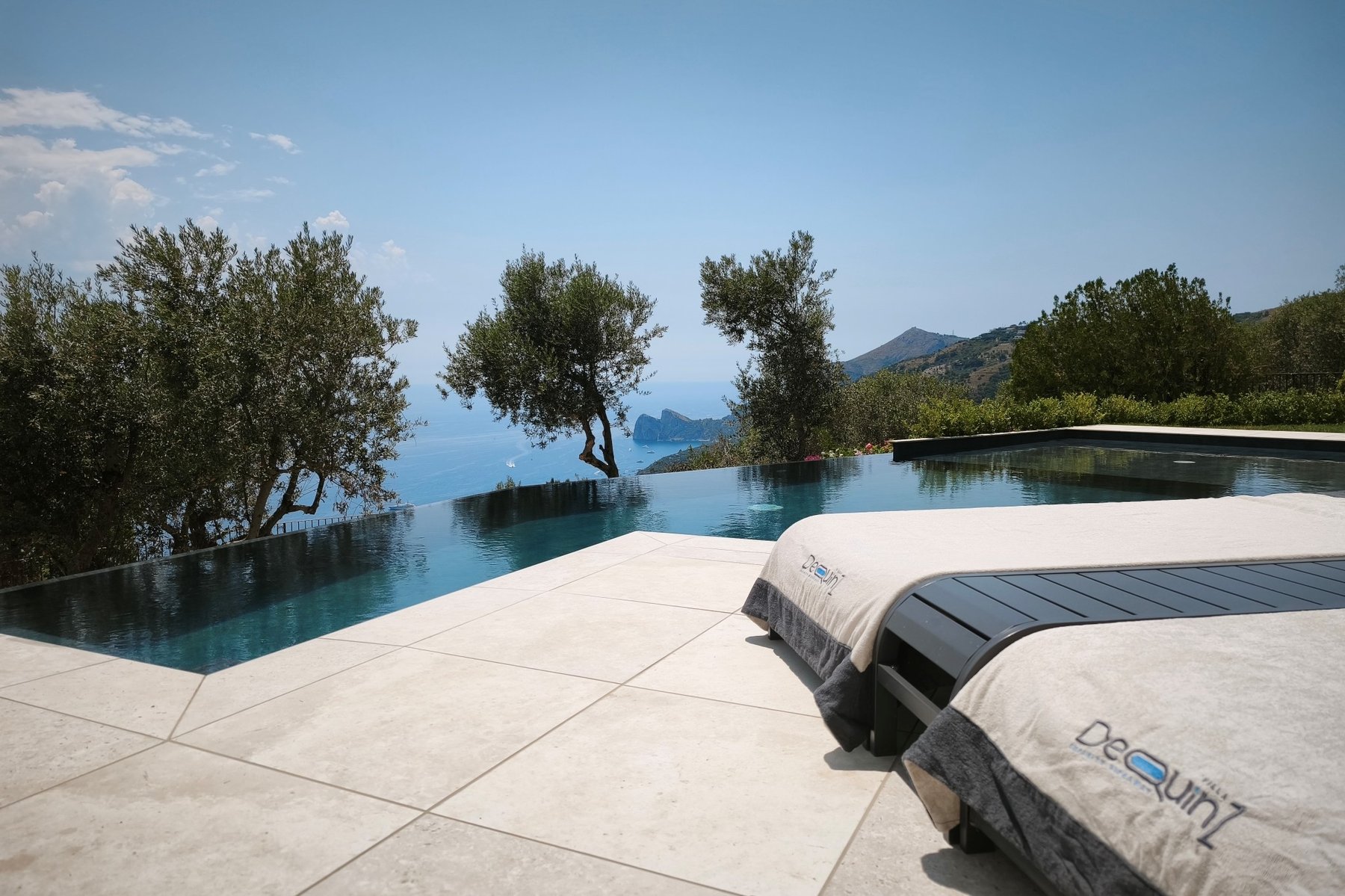 Piscina a sfioro con lettini e vista sul mare tra gli ulivi