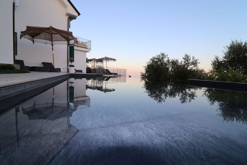 Piscina a sfioro al crepuscolo con ombrelloni e la villa illuminata