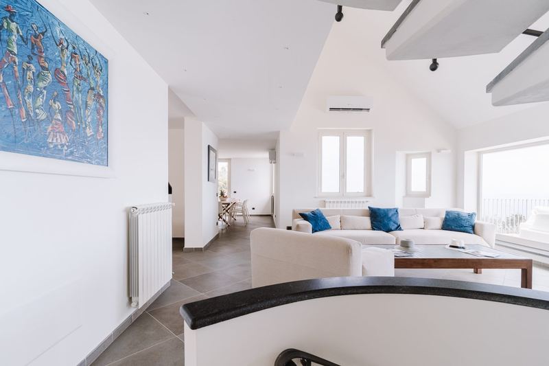 Salone con quadro d'autore, divani chiari e vetrate sul mare
